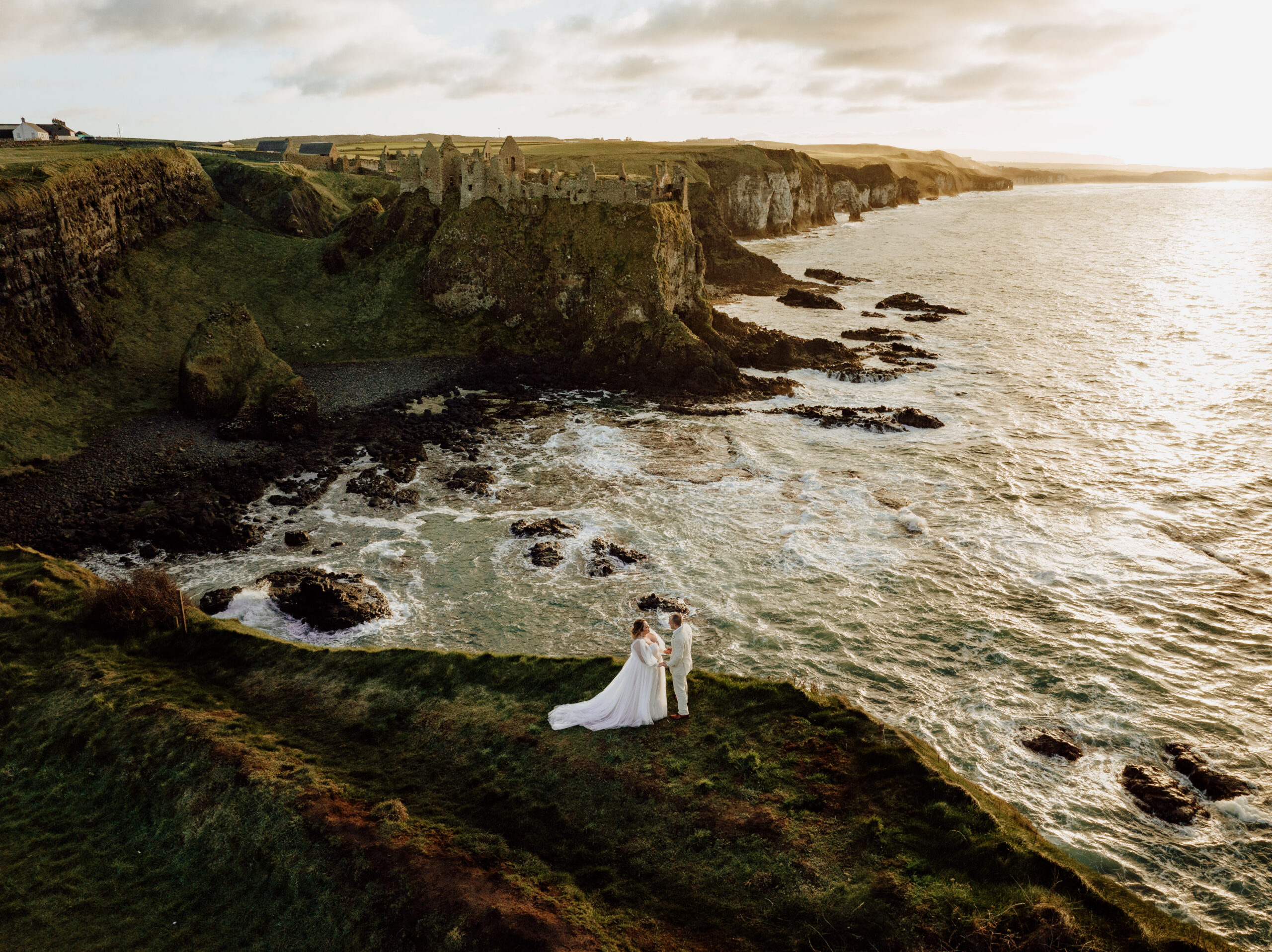 couple on cliff edge overlooking dunluce castle and the sea