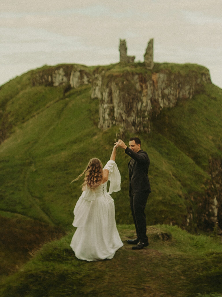 A young couple with a beautiful dress doing a dance at dunseverick castle ruins in the background